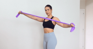 Mulher fazendo alongamento com faixa elástica acima da cabeça, ilustrando o tema “alongar antes ou depois do treino”.