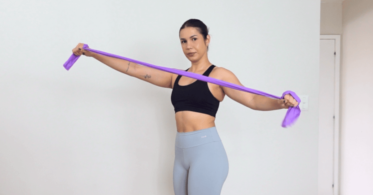 Mulher fazendo alongamento com faixa elástica acima da cabeça, ilustrando o tema “alongar antes ou depois do treino”.